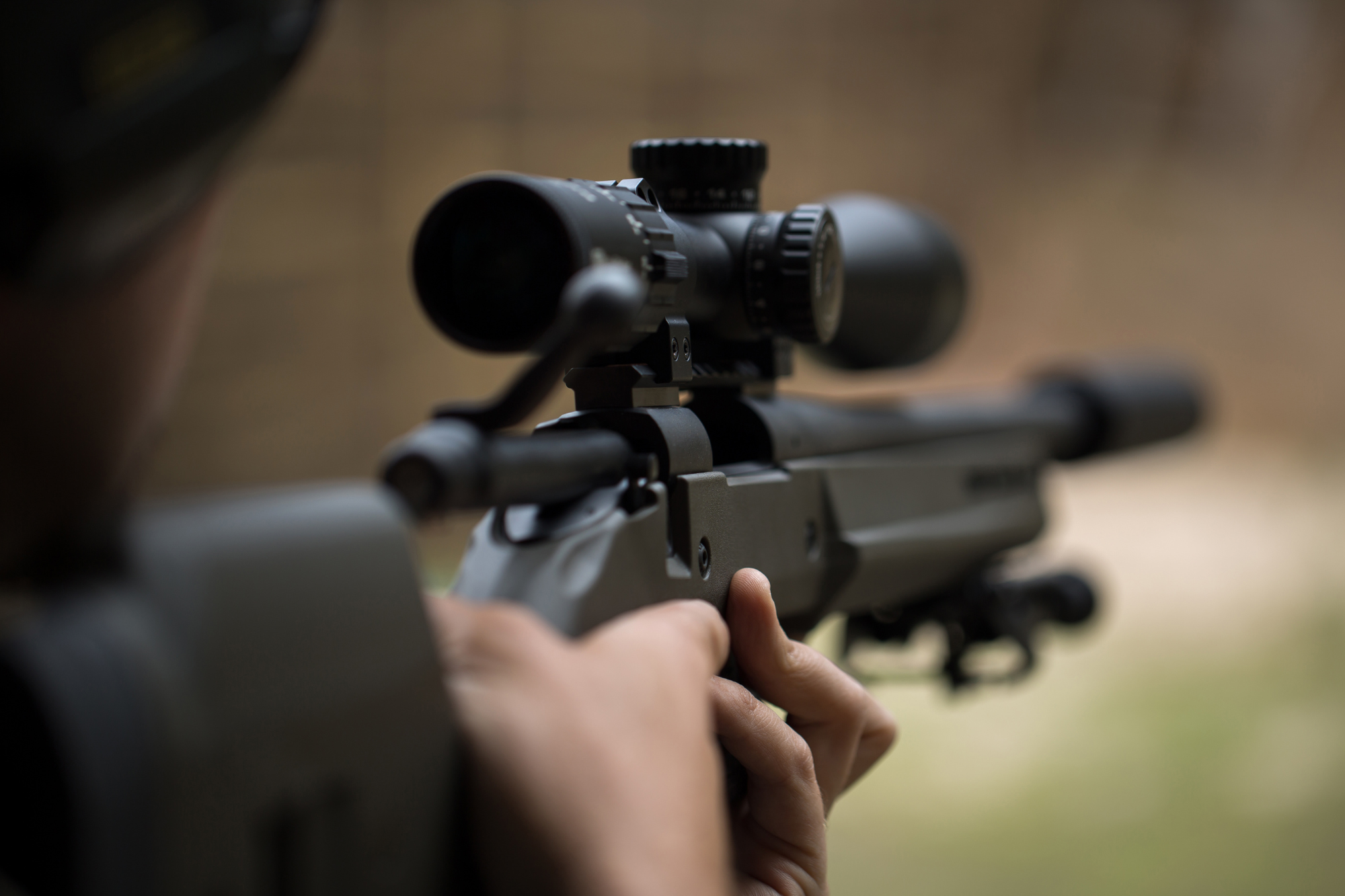 A hunter aiming a scoped rifle at a distant target, with a blurred background.